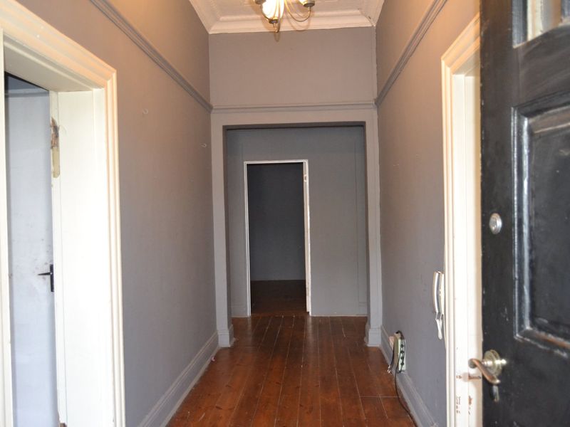 A vacant hallway featuring timber flooring, decorative cornicing, and neutral grey walls, providing access to multiple rooms within the home.