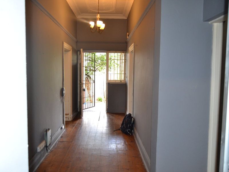 A spacious hallway featuring original hardwood flooring, ornate ceiling detailing, and direct access to the exterior through a security gate.