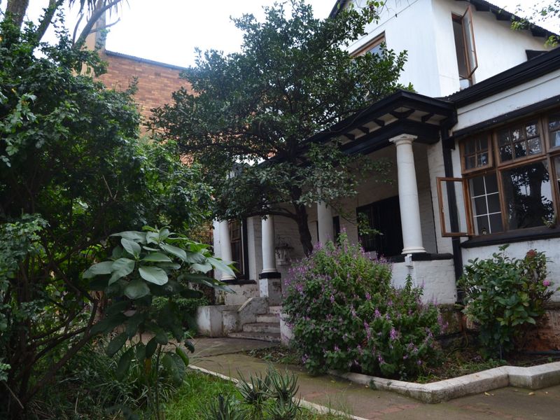 Front elevation of a character home featuring a covered porch with classical columns, mature garden landscaping, and traditional timber-framed windows.