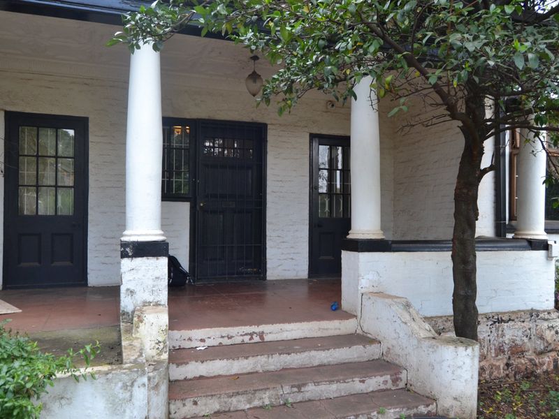 Front entrance featuring a covered porch with decorative columns, concrete steps, and multiple timber-framed doors with security gates.