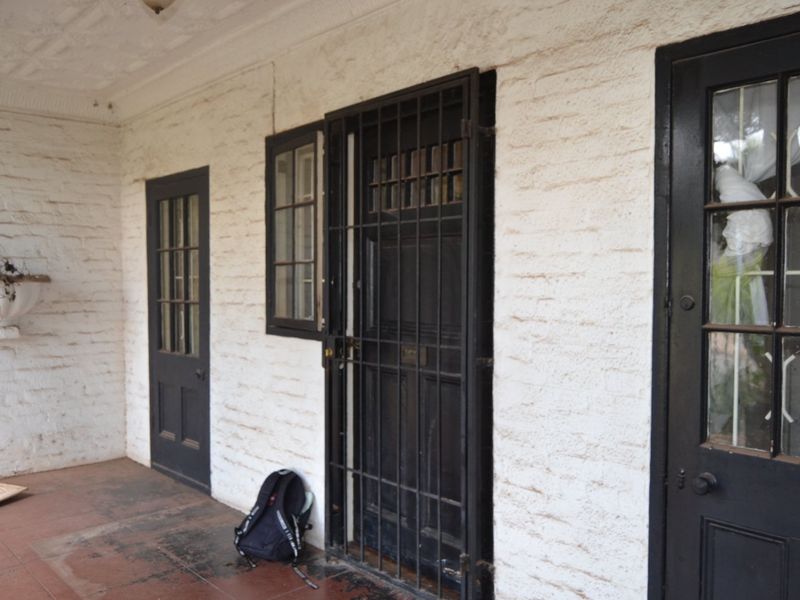 A covered patio area featuring painted brick walls, tiled flooring, and multiple timber-framed access doors with security gates.