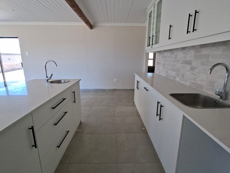 Modern kitchen featuring white shaker cabinetry, quartz countertops, dual sinks, and a distinctive exposed timber beam against a tongue and groove ceiling.