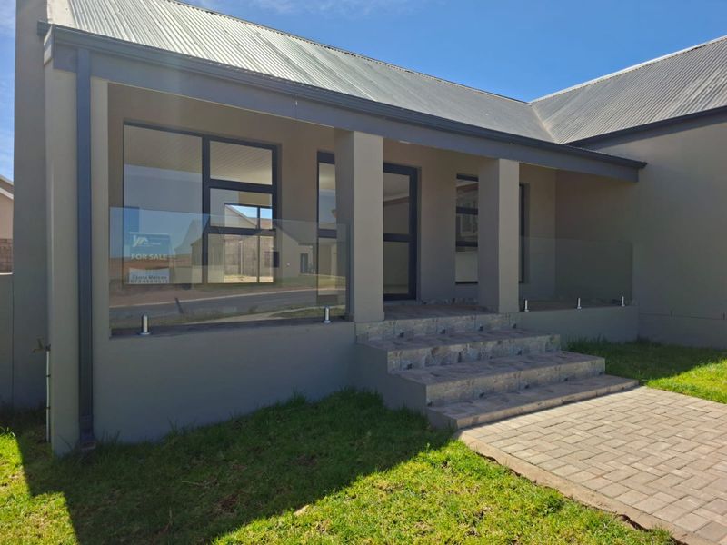 Front facade of a modern house featuring a covered entrance, glass balustrade, tiled steps, and paved walkway.
