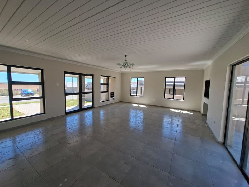 Spacious, light-filled living area featuring large aluminium windows, sliding doors, tiled flooring, and a built-in fireplace, offering a blank canvas for interior design.