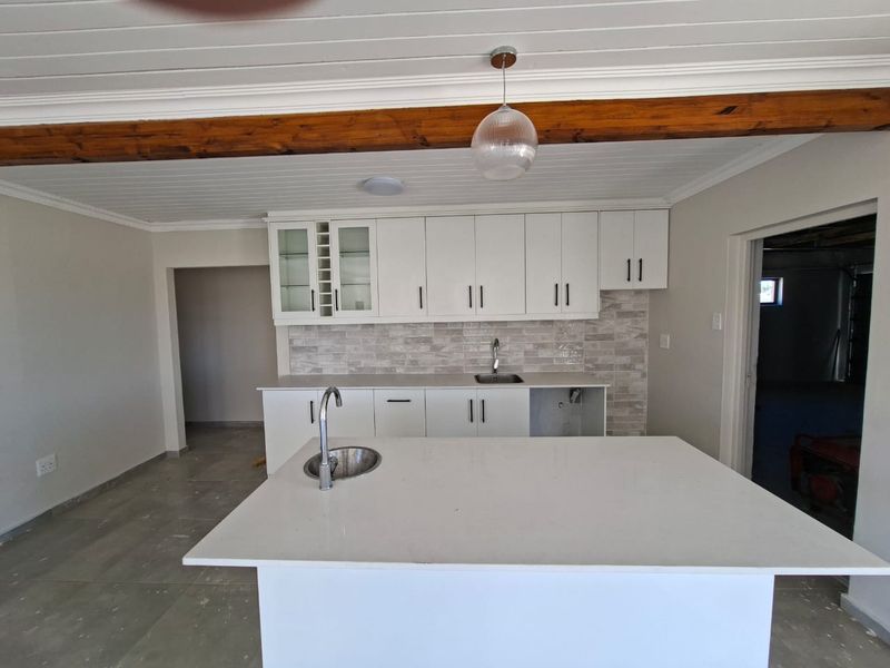 Modern kitchen featuring white shaker cabinetry, quartz countertops, a central island with sink, and a stylish tiled backsplash under a timber-accented ceiling.