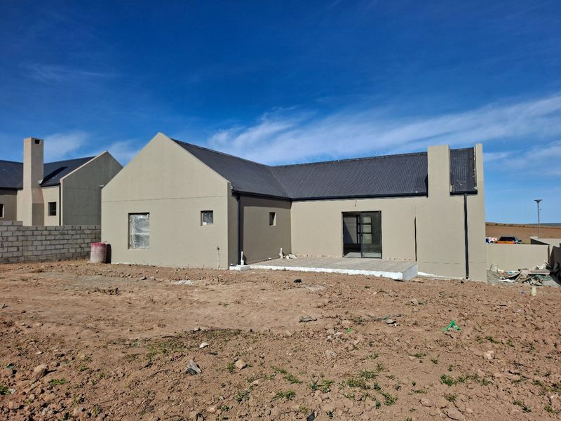 Rear view of a newly constructed house featuring a corrugated metal roof, plastered exterior walls, and a concrete patio area awaiting landscaping.
