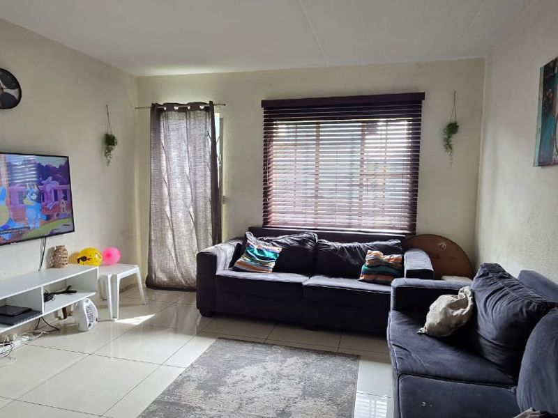 A living room featuring tiled flooring and venetian blinds, providing a functional space with potential for cosmetic updates to the wall finishes.
