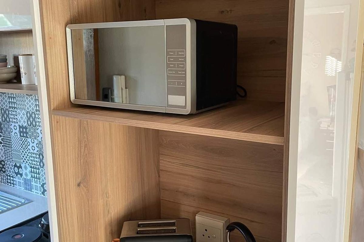 A modern kitchen nook featuring wood-grain cabinetry, open shelving, and a decorative patterned tile splashback, providing a functional and stylish prep area.