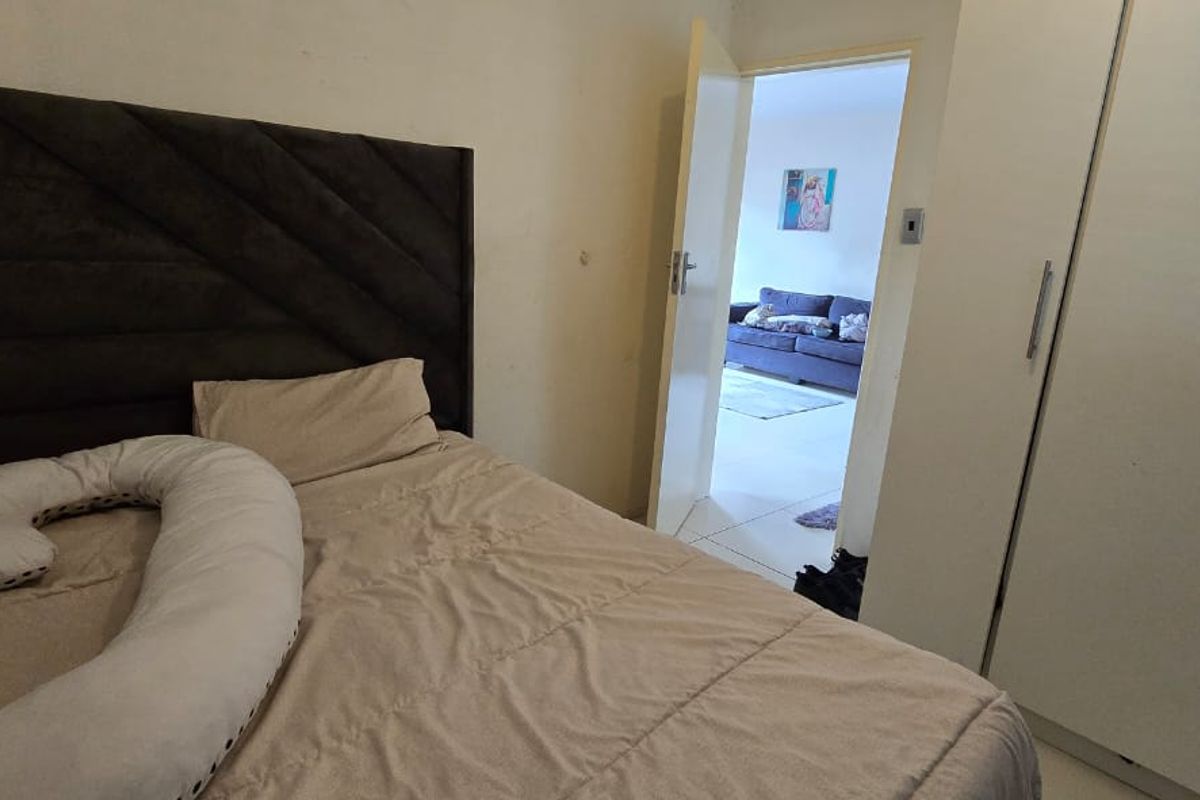 A bedroom featuring a built-in wardrobe and access to an adjacent living area, showing signs of wear on the wall surfaces.