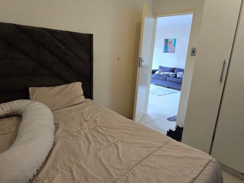 A bedroom featuring a built-in wardrobe and access to an adjacent living area, showing signs of wear on the wall surfaces.