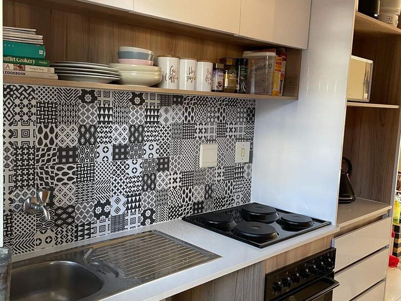 Modern kitchen featuring a striking patterned tile backsplash, built-in electric hob, oven, and ample cabinetry with integrated open shelving for storage.