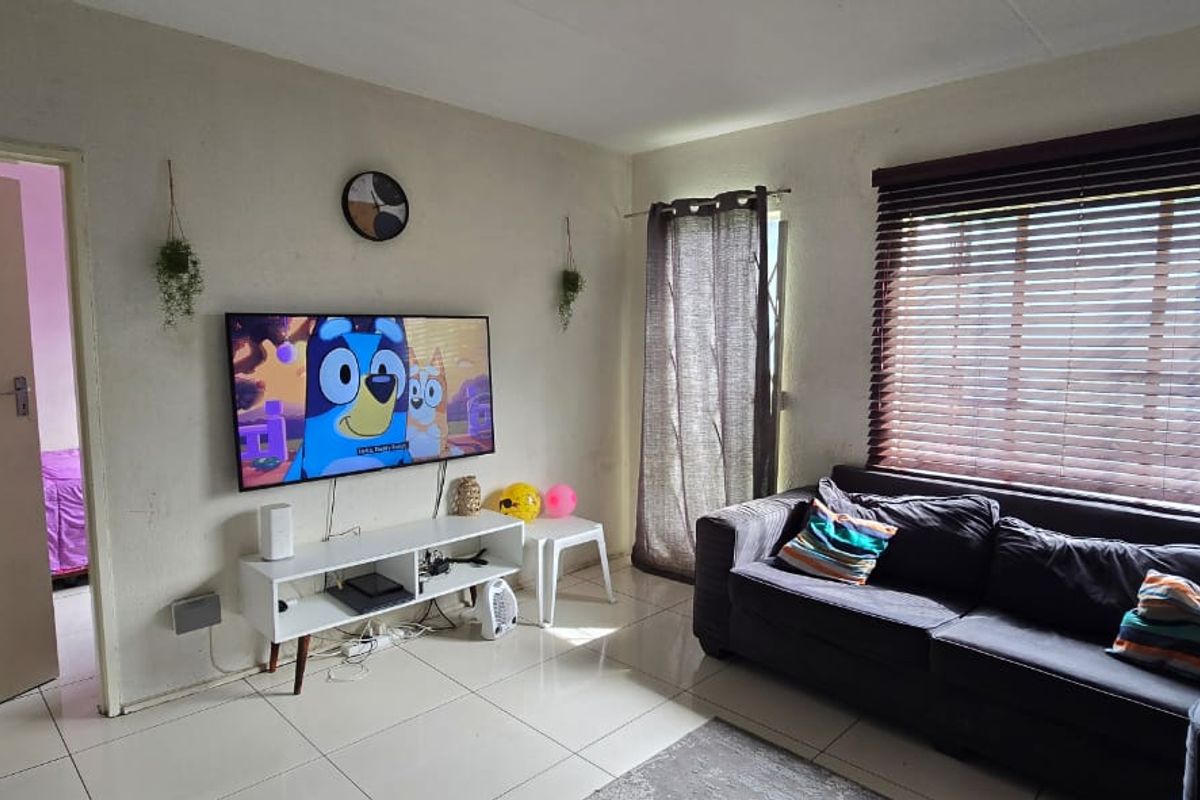 A living room featuring tiled flooring and venetian blinds, providing a functional space with potential for cosmetic updates to the wall finishes.