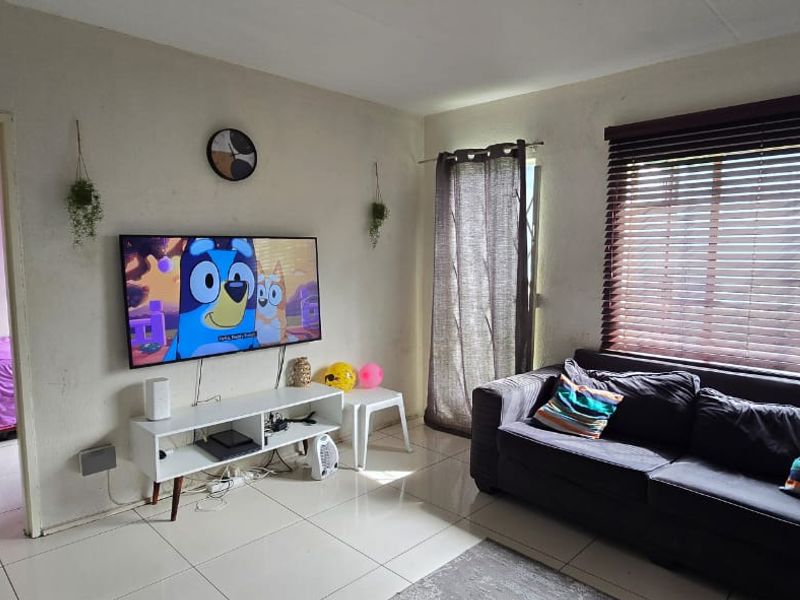 A living room featuring tiled flooring and venetian blinds, providing a functional space with potential for cosmetic updates to the wall finishes.