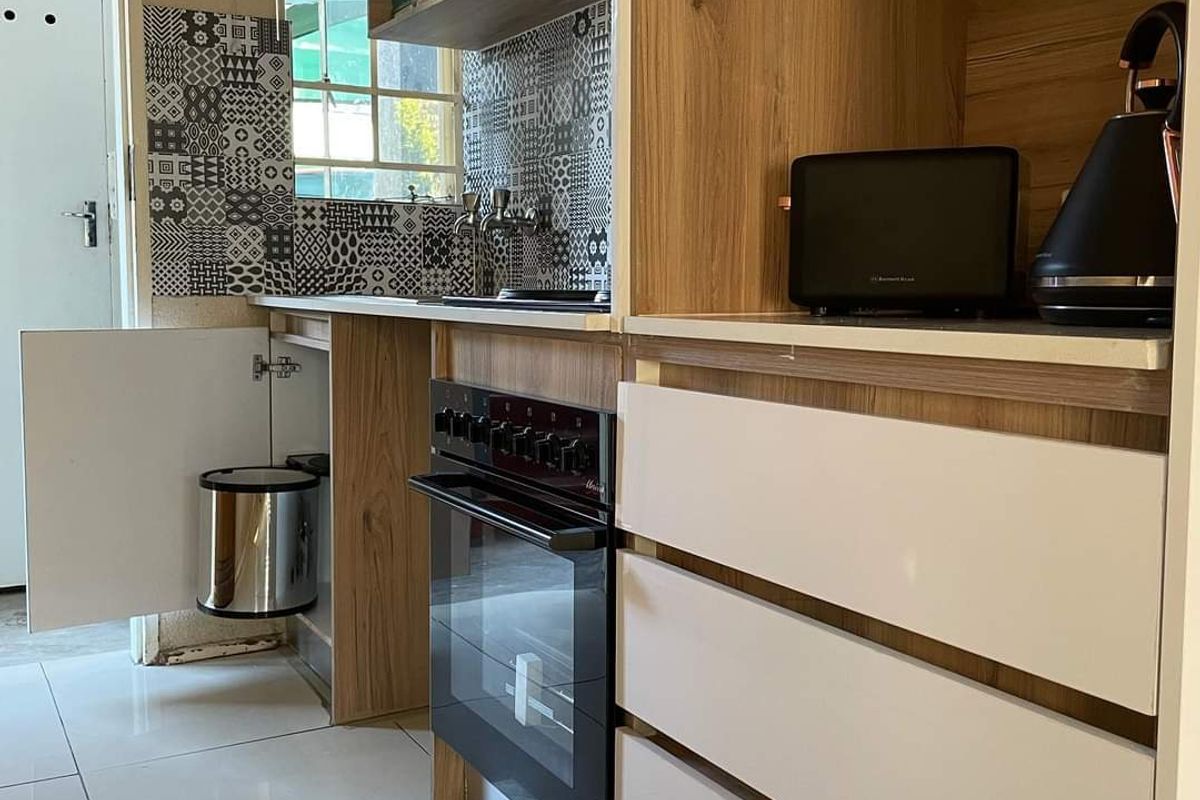 Compact kitchen featuring modern wood-look cabinetry, a built-in oven, patterned tiled backsplash, and white floor tiles.