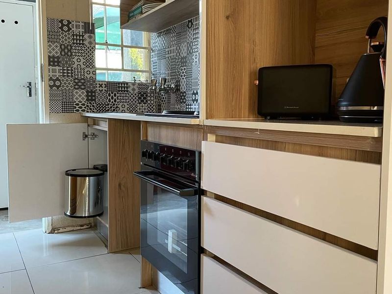 Compact kitchen featuring modern wood-look cabinetry, a built-in oven, patterned tiled backsplash, and white floor tiles.