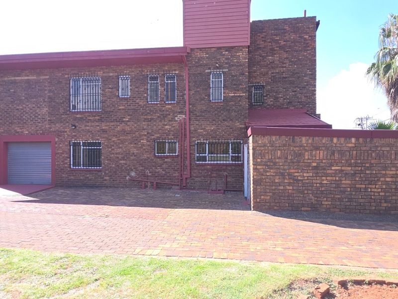Front exterior view of a face brick house featuring a paved driveway, secure roller shutter garage, and perimeter walling with security fencing.
