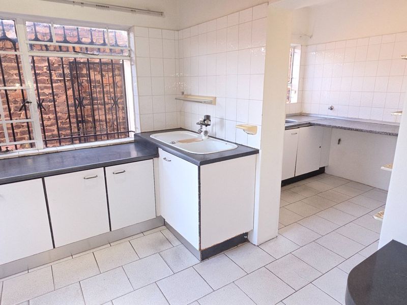 A functional, empty kitchen featuring white cabinetry, dark laminate countertops, tiled splashbacks, and tiled flooring, ready for modernization.