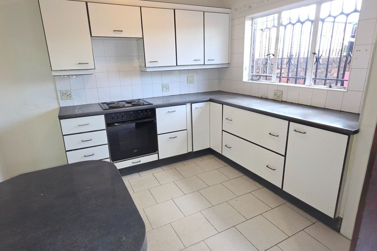 A functional kitchen featuring white built-in cabinetry, dark laminate countertops, an integrated electric oven and hob, and tiled flooring.