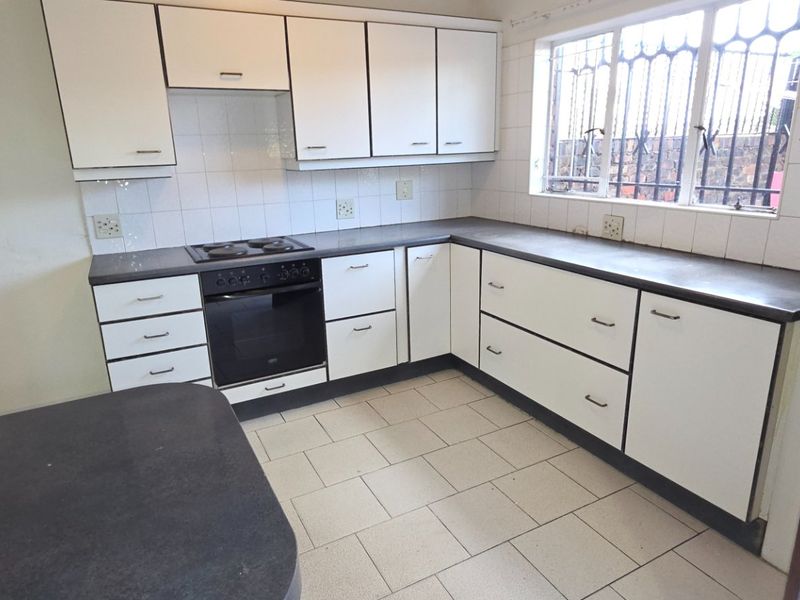 A functional kitchen featuring white built-in cabinetry, dark laminate countertops, an integrated electric oven and hob, and tiled flooring.