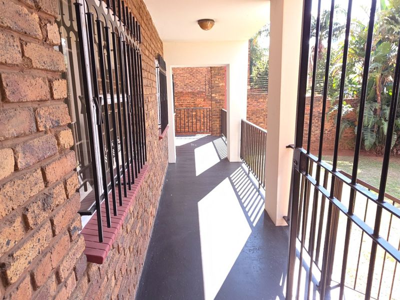 A covered outdoor patio area featuring exposed brick walls, security bars, and a painted concrete floor overlooking the garden.