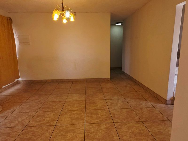 An empty, open-plan living area featuring neutral walls and ceramic floor tiles, providing a blank canvas for interior design.