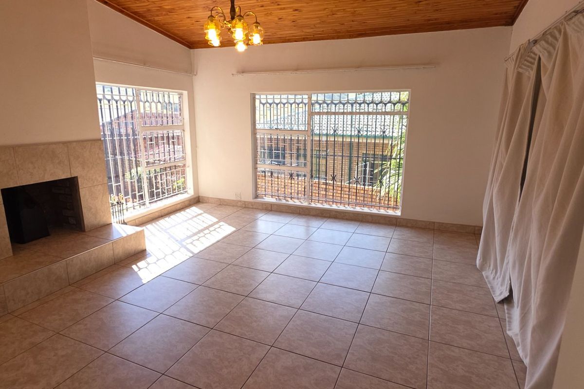 Spacious living room featuring tiled flooring, a tiled fireplace, and a timber ceiling, offering a bright and open area for relaxation.