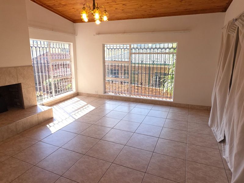 Spacious living room featuring tiled flooring, a tiled fireplace, and a timber ceiling, offering a bright and open area for relaxation.