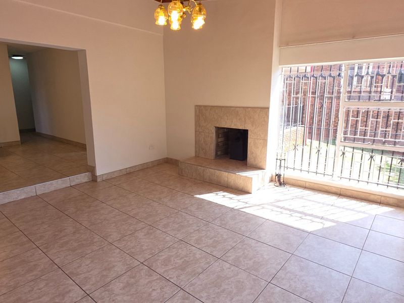 Spacious, tiled living area featuring a built-in fireplace and large windows with security bars, offering a bright and open layout.