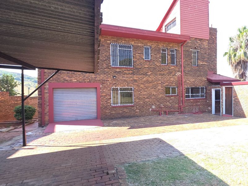 Rear view of a face brick house featuring a paved driveway, integrated garage with a roller door, and a covered carport area.