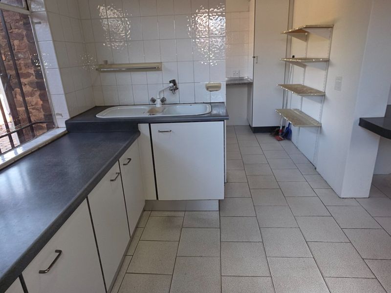 A functional, empty kitchen featuring laminate countertops, a double sink, tiled splashback, and ceramic floor tiles, offering a blank canvas for renovation.