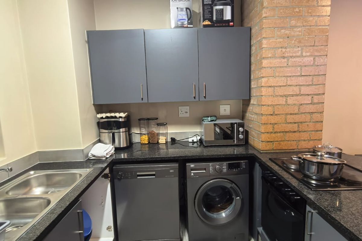 A functional kitchen featuring dark grey cabinetry, granite countertops, a double sink, and integrated appliances including a dishwasher, washing machine, and built-in oven.
