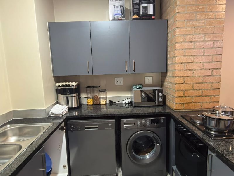A functional kitchen featuring dark grey cabinetry, granite countertops, a double sink, and integrated appliances including a dishwasher, washing machine, and built-in oven.