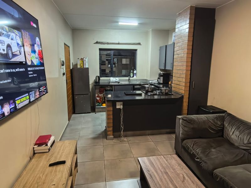 Open-plan living area featuring a compact kitchen with built-in cabinetry, hob, and tiled flooring, seamlessly connected to the lounge space.
