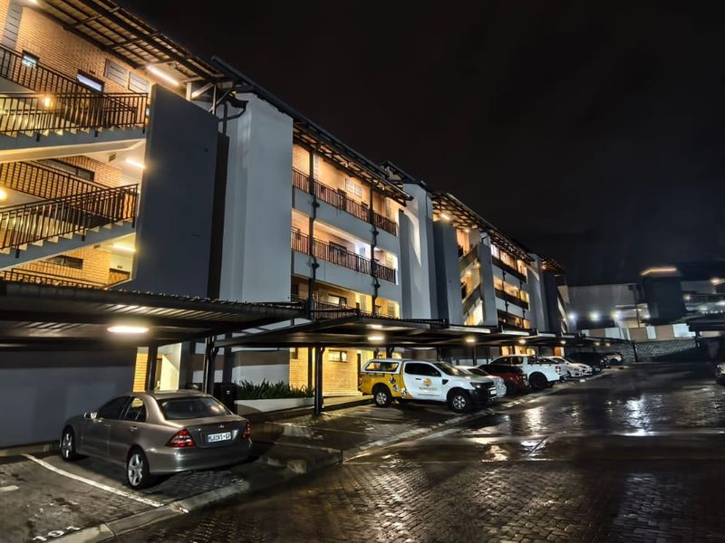 Night view of an apartment complex featuring multi-level balconies, external stairwells, and covered parking bays with paved driveway access.