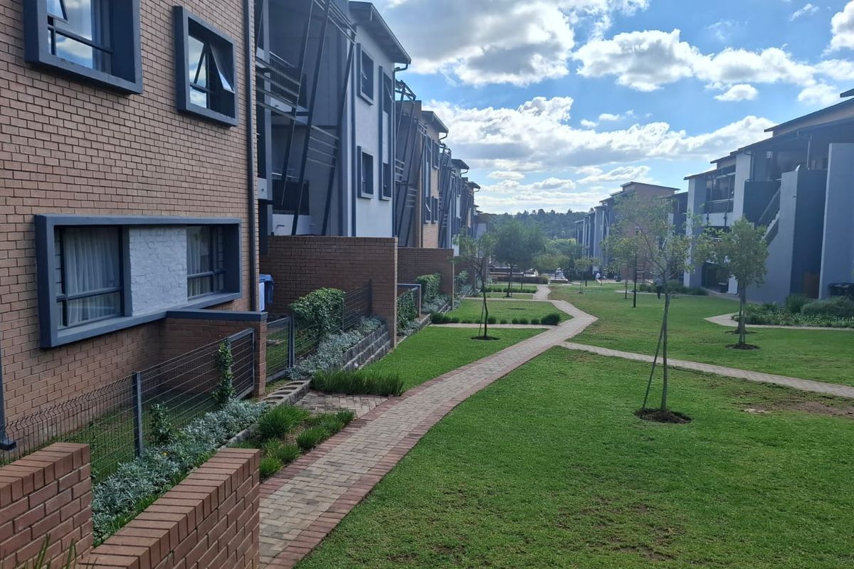 A view of the rear exterior of the apartment complex, featuring brick facades, paved walkways, and well-maintained communal garden areas.