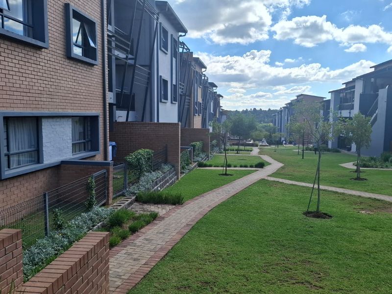 A view of the rear exterior of the apartment complex, featuring brick facades, paved walkways, and well-maintained communal garden areas.