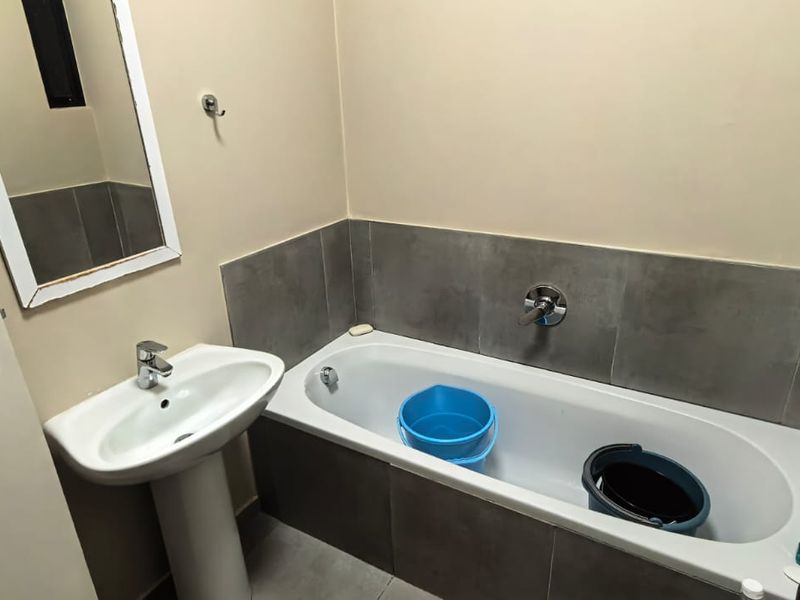 A functional bathroom featuring a pedestal basin, a bathtub with wall-mounted fixtures, and neutral grey wall tiling.