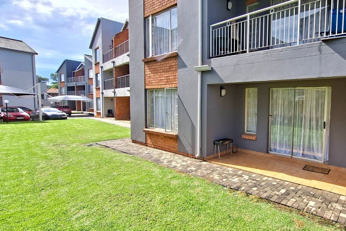 Ground floor apartment exterior featuring a private tiled patio, sliding glass doors, and access to a well-maintained communal garden area.