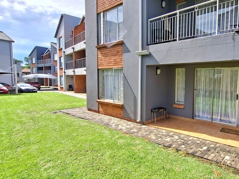 Ground floor apartment exterior featuring a private tiled patio, sliding glass doors, and access to a well-maintained communal garden area.