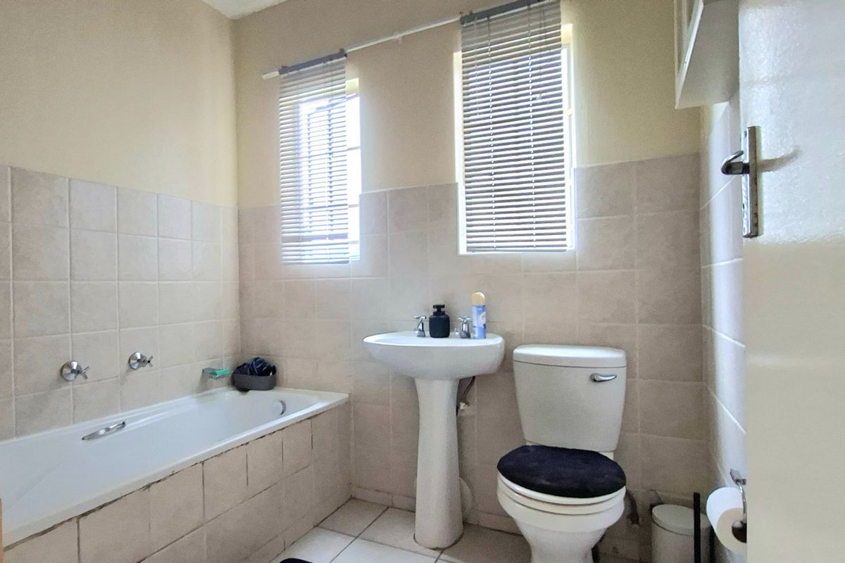 A functional bathroom featuring a pedestal basin, bathtub, and toilet with neutral wall and floor tiling.