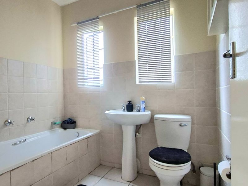 A functional bathroom featuring a pedestal basin, bathtub, and toilet with neutral wall and floor tiling.
