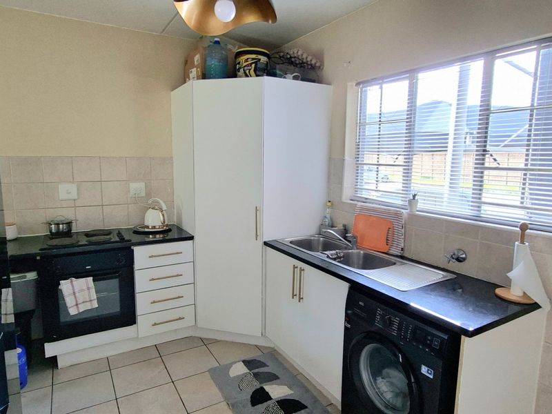 A functional kitchen featuring built-in cabinetry, a black electric hob and oven, double sink, tiled splashback, and tiled flooring.
