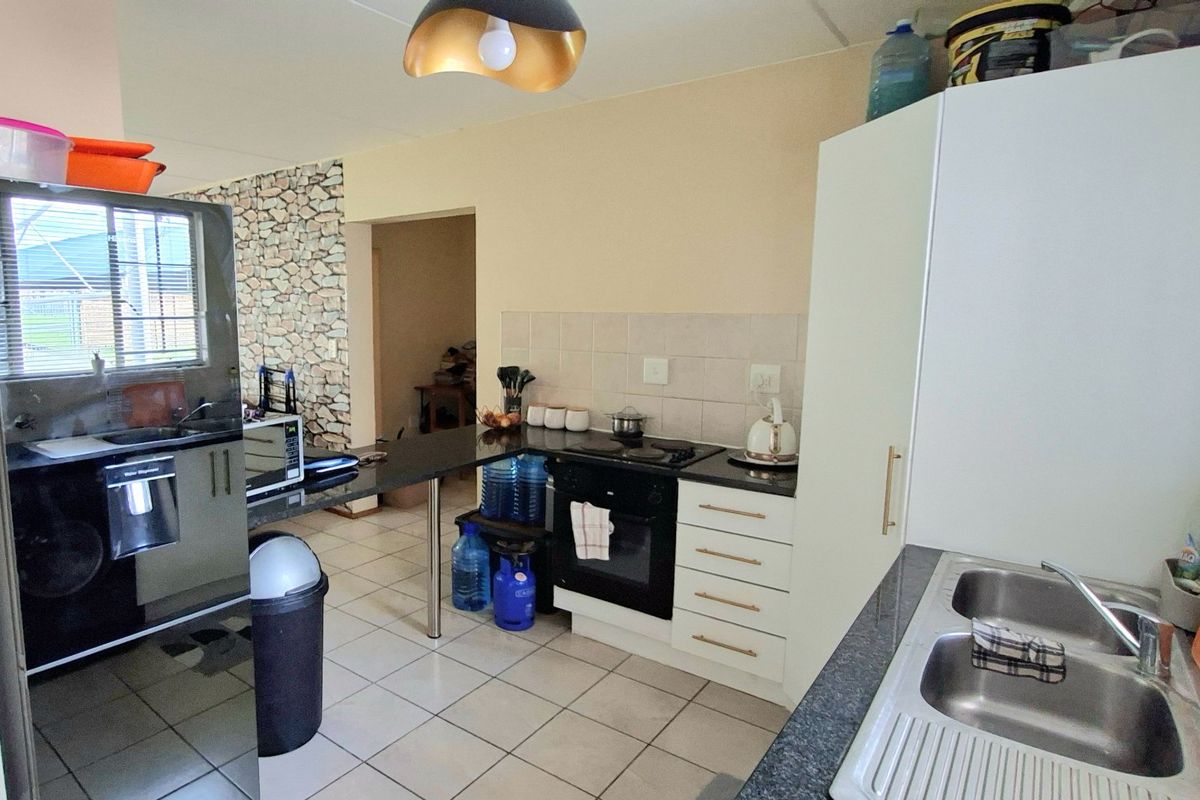 Functional kitchen featuring built-in cabinetry, electric oven and hob, double stainless steel sink, and tiled flooring with a decorative stone-look feature wall.