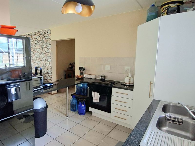 Functional kitchen featuring built-in cabinetry, electric oven and hob, double stainless steel sink, and tiled flooring with a decorative stone-look feature wall.