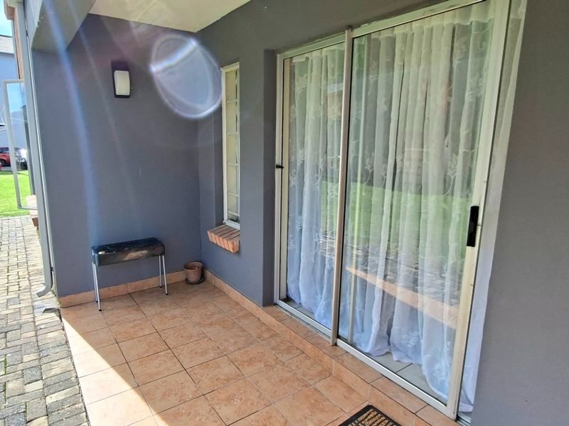 A covered patio area featuring tiled flooring and a sliding glass door providing access to the interior of the apartment.