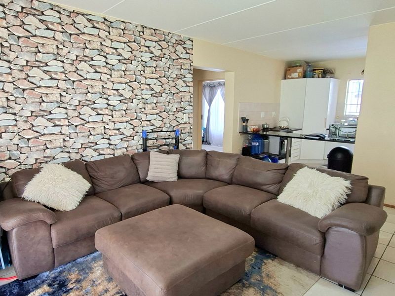 Open-plan living area featuring a stone-effect feature wall, tiled flooring, and an adjoining kitchen with a breakfast bar.
