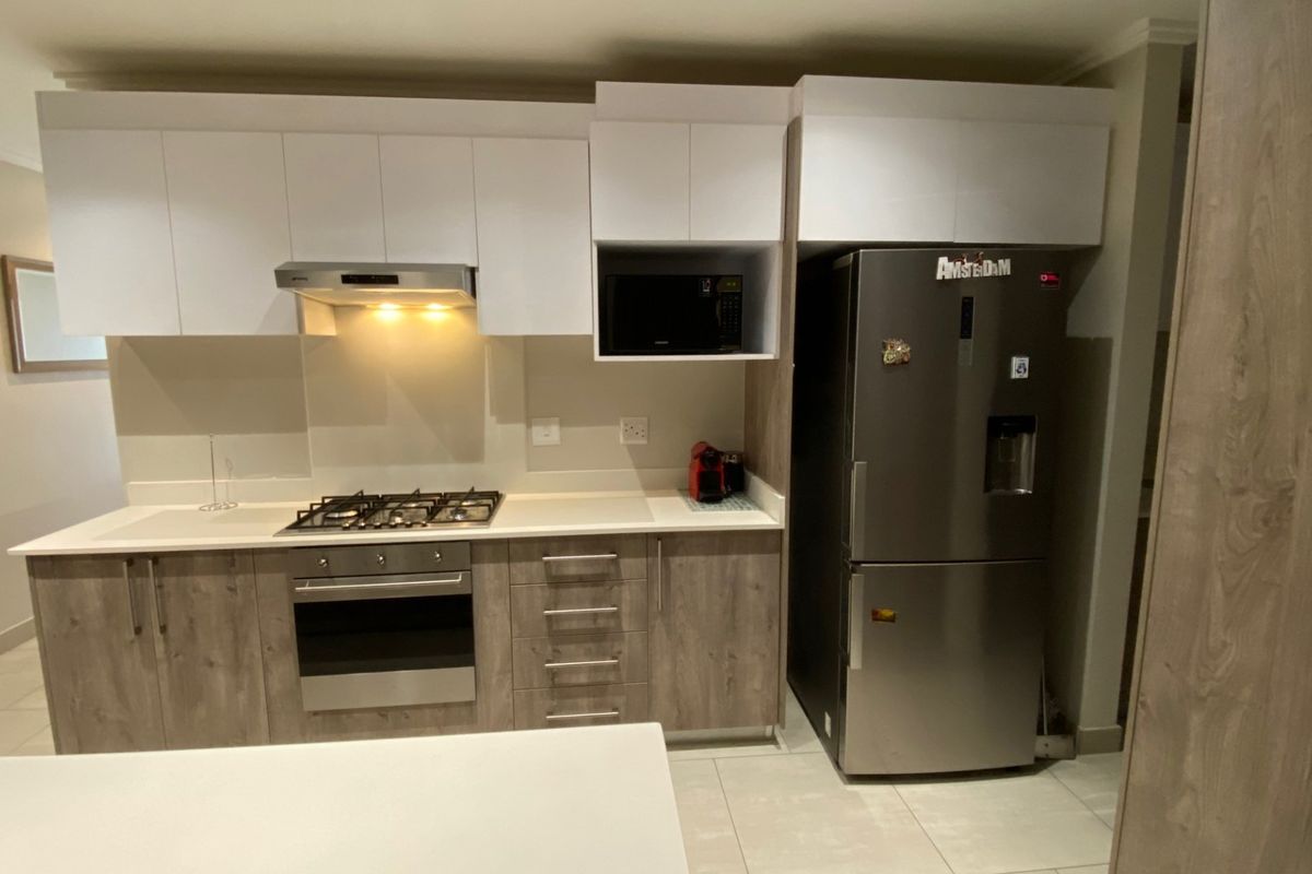 Modern kitchen featuring white and wood-grain cabinetry, stone countertops, gas hob, built-in oven, and integrated extractor fan.