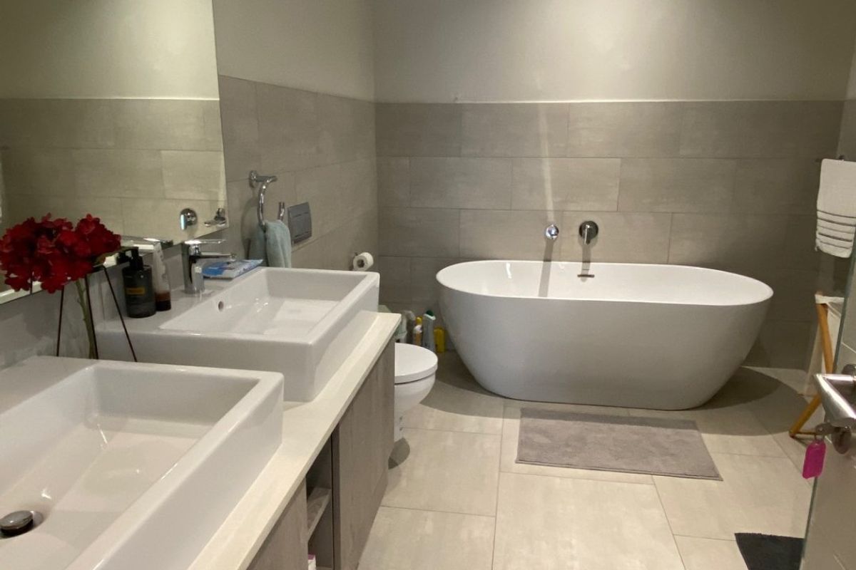 Modern bathroom featuring a double vanity with vessel sinks, a sleek freestanding bathtub, and neutral large-format floor tiles.