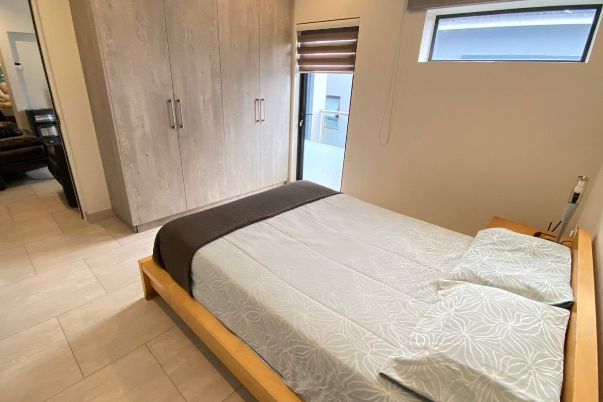 A well-maintained bedroom featuring modern built-in cupboards, neutral tiled flooring, and a high-level window with roller blinds.