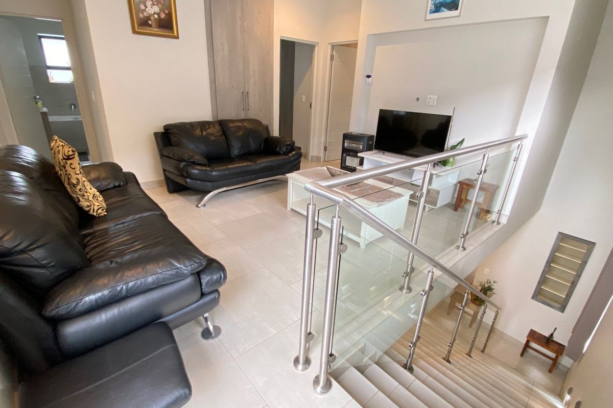 Open-plan living area featuring modern tiled flooring and a contemporary stainless steel and glass staircase balustrade overlooking the lower level.